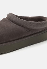 Dark gray suede slip-on shoe with a textured collar and a thick, serrated rubber sole. Features subtle logo detailing on the side.