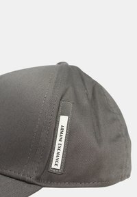 Cappello grigio in tessuto con una texture liscia, dotato di un'etichetta logata cucita di lato e un design strutturato.