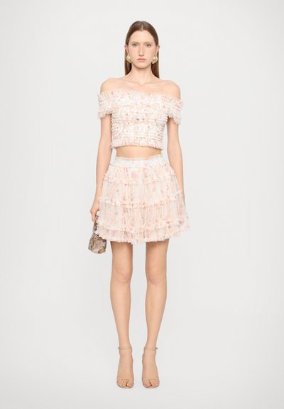 Top scurt roz, cu umerii goi, și fustă mini cu straturi, realizate dintr-un material transparent cu volane. Are un corset ajustat și un tiv stratificat, evazat.