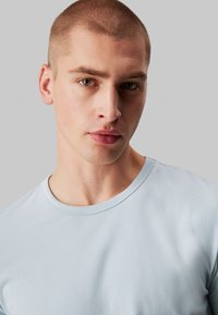 Light blue short-sleeve t-shirt, round neck, smooth cotton fabric, minimalistic design, showcased on a model with a neutral background.