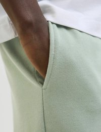 Lichtgroene katoenen joggers met een zichtbare zijzak en een gestructureerde stof, gecombineerd met een witte bovenkleding. Close-up weergave.