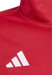 Rotes Sportoberteil mit hohem Kragen. Verfügt über ein weißes Drei-Streifen-Logo, strukturierten Stoff und glatte Nähte.