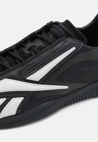 Scarpa sportiva nera con tomaia in tessuto testurizzato, dettagli bianchi e design con lacci. Presenta una suola in gomma con un motivo antiscivolo.