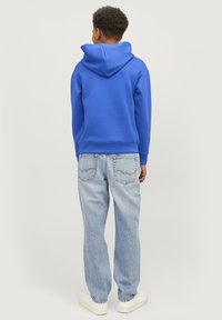 Modrá mikina s klokánkovou kapsou a kapucí na šňůrku, spárovaná se světle modrými džínami. Bílé tenisky dotvářejí celkový vzhled.