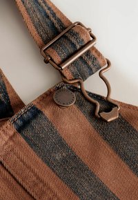 Brun og blåstribet stof med en metalclipslås og en rund knap med tekst. Teksturen er denim-lignende.