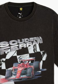 Hanorac negru din bumbac, cu inscripția "SCUDERIA FERRARI" în text argintiu și un grafic cu o mașină de Formula 1 roșie pe un fundal pătrățel.