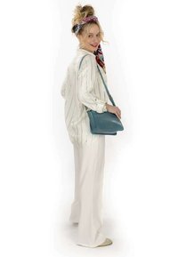 Chemise blanche à manches longues avec des rayures bleues, pantalon large blanc, et un sac à main texturé couleur teal. Modèle coiffé d'un foulard coloré.