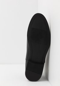 Chaussure noire avec dessus en cuir lisse, semelle plate et talon en caoutchouc texturé, affichant la taille 42 sur la semelle intérieure.