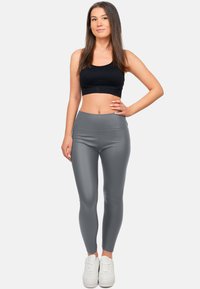 Leggings grigi con tuta aderente, dalla superficie liscia e con vita alta, abbinati a un top corto nero e sneakers bianche.