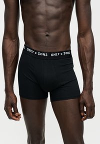 Male torso wearing black boxer briefs with "ONLY & SONS" text on the waistband, showing muscular arms and abdomen.