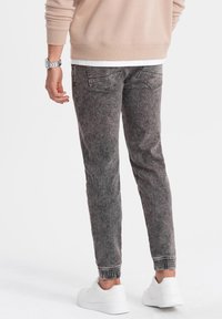 Bleka svarta denim joggerbyxor med ribbade muddar, bakfickor och en avslappnad passform, kombinerat med vita sneakers och en beige sweatshirts.