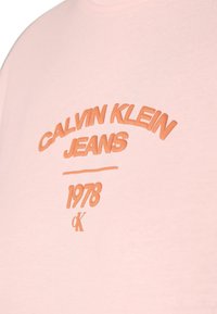 Růžové bavlněné tričko s vyvýšeným oranžovým textem: "CALVIN KLEIN JEANS 1978" a stylizovaným logem 'CK'. Kulatý výstřih, hladká textura.