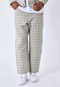 Pantalones beige con un diseño geométrico de diamantes, corte de pierna ancha y material textil suave, combinados con zapatillas blancas.