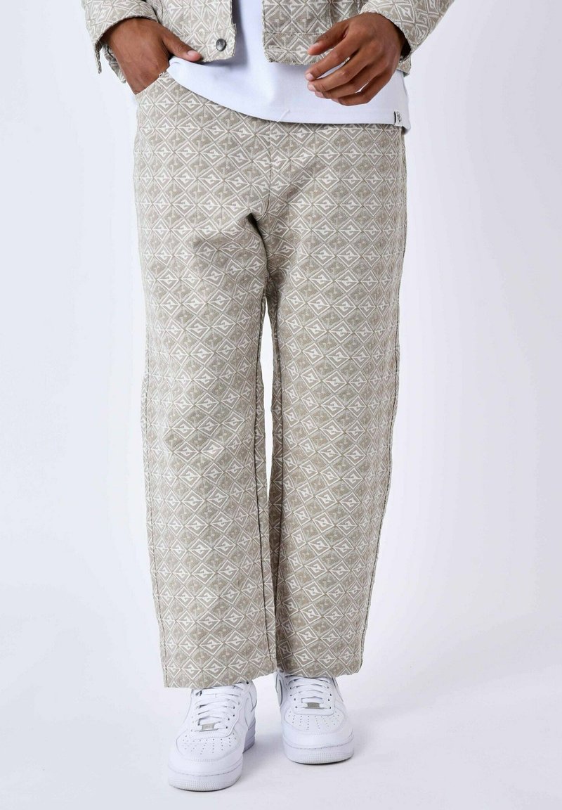 Pantalones beige con un diseño geométrico de diamantes, corte de pierna ancha y material textil suave, combinados con zapatillas blancas.