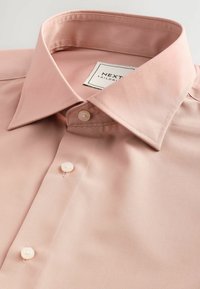 Lichtroze shirt met korte mouwen, zachte textuur, puntkraag en twee parelmoer knopen bij de hals, gelabeld "NEXT TAILORED."