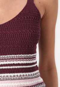 Top en tricot bordeaux avec un haut texturé et des rayures horizontales en blanc et rose clair. Le tissu a une maille ouverte et un design ajusté.