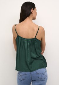 Temnozeleni satenski top s tankimi naramnicami, nastavljivimi trakovi, elastičnim hrbtom in ohlapnim krojem. Usklajen z svetlo modrimi kavbojkami.