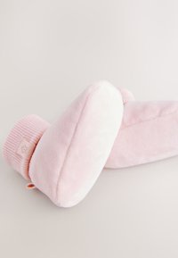 Chaussons roses doux avec un extérieur en peluche, un bord côtelé rose et un emblème floral discret. Forme arrondie et semelle plate pour le confort et la chaleur.