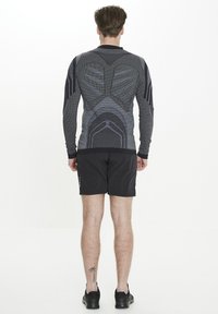 Långärmad atletisk topp i svart och grått med strukturerad design och slimmad passform. Kombinerad med svarta shorts och atletiska skor.