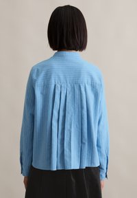 Lichtblauwe button-up shirt met verticale witte strepen, een geplooid achterontwerp en lange mouwen met manchetknopen. Geschikt voor casual wear.