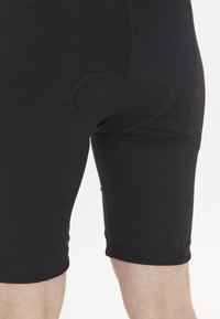 Schwarze Kompressionsshorts mit glatter Textur, ausgestattet mit einem konturierten Rückenpanel und gestickten Akzenten. Abgeschnittene Säume am Oberschenkel.