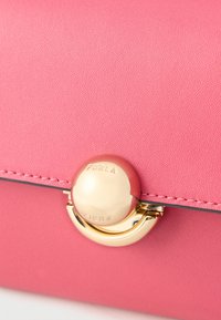 Rózsaszín Furla bőrtáska texturált kivitelben, aranyszínű kerek kapoccsal és varrással az éleken.