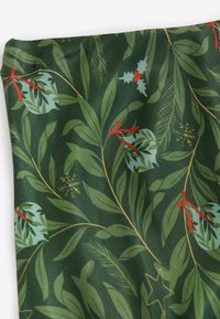 Tissu vert avec un motif botanique comprenant des feuilles, des rubans rouges et des ornements de Noël, rehaussé de détails dorés et blancs.