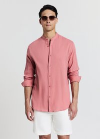 Light pink long-sleeve shirt with a band collar, button front, textured fabric, and rolled sleeves, paired with white shorts.