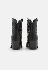 Černé kotníkové boty z kůže s blokovým podpatkem, zdobené prošitými vzory ve tvaru šipky a poutky pro snadné obouvání. Hladká textura s elegantním designem.