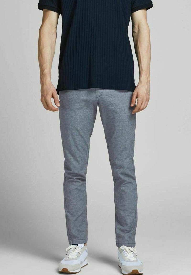 Czarna podkoszulka z ribbingu w połączeniu z jasnoszarymi, dopasowanymi spodniami i białymi trampkami. Skupienie na casualowym, nowoczesnym wzornictwie i gładkich teksturach.