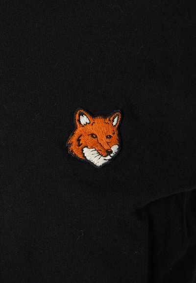 Black fabric t-shirt featuring a small orange and white embroidered fox head on the left chest area. Textured and detailed stitching visible.