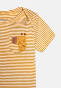 Chemise à manches courtes rayée jaune et blanche avec un design de poche en forme de girafe. Fabriquée en tissu doux avec un col rond.