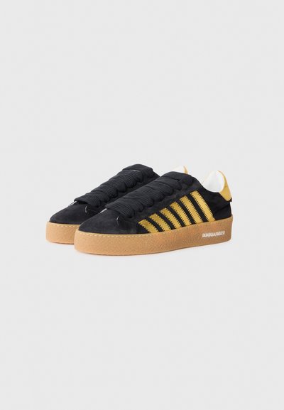 Black suede sneakers with yellow stripes, textured rubber sole, and black laces. Features a white logo on the side and yellow accents at the heel.