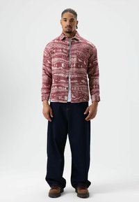 Rood-wit geruit flanellen overhemd met een knoopsluiting aan de voorkant, gecombineerd met marineblauwe wijde broekspijpen en bruine veterlaarzen. Details van de gestructureerde stof zijn zichtbaar.