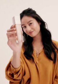 Bouteille en verre transparent avec un capuchon argenté tenue par une personne. La bouteille contient un liquide d'une teinte beige clair. La personne porte un haut de couleur moutarde.