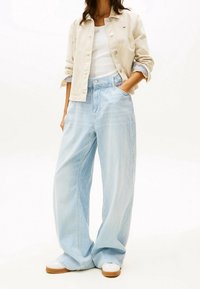 Chaqueta beige clara sobre una blusa blanca, combinada con pantalones de rayas azules y blancas de pierna ancha, con un ajuste relajado y bolsillos laterales.