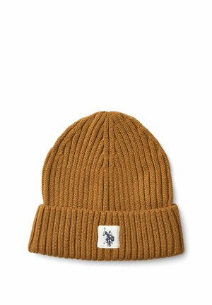 Jeune femme portant un bonnet en laine moutarde et une écharpe assortie avec une veste marron, souriant doucement sur un fond uni.