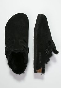 Mustad suede plätud ümmarguse kujuga, millel on hebelrihm ja pehme vooder. Libisemisvastane kummist tald brändi logo detailiga.
