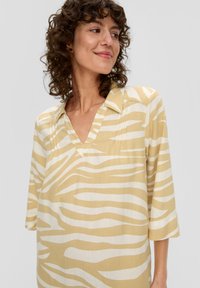 Gestreiftes Shirt in Gelb und Weiß mit V-Ausschnitt, Dreiviertelärmeln und relaxed Fit, mit einer linnenartigen Textur.