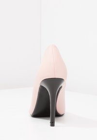 Rosa högklackad sko med spetsig tå, slät läderöverdel och en blanka svart stilettklack. Sömmar vid baksidan.