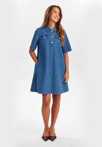 Robe en denim bleu à pois blancs, manches courtes, col et détails de boutons, avec des poches latérales et une jupe évasée.