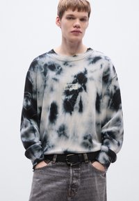 Ανάλαφρο πουλόβερ με σχέδιο tie-dye, που περιλαμβάνει αποχρώσεις του μαύρου και του λευκού. Ριμπ μανσέτες, στρογγυλή λαιμόκοψη και επώνυμη ετικέτα στο κέντρο.