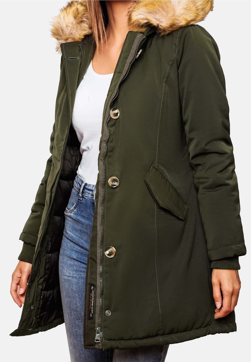 Parka femme vert foncé avec capuche bordée de fourrure, fermeture à boutons et zip, portée sur un haut blanc et un jean bleu.