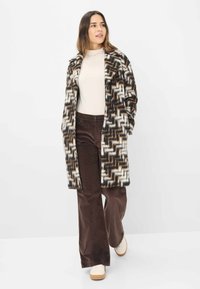 Patroon oversized jas in bruin, crème en zwart; heeft een zigzagontwerp, open voorkant en zijzakken. Gecombineerd met bruin corduroy broeken.