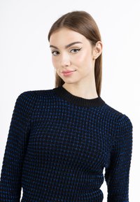 Maglione nero con un motivo a scacchi testurizzato e accenti blu. Collo e polsini a coste. Vestibilità elegante e maniche lunghe.