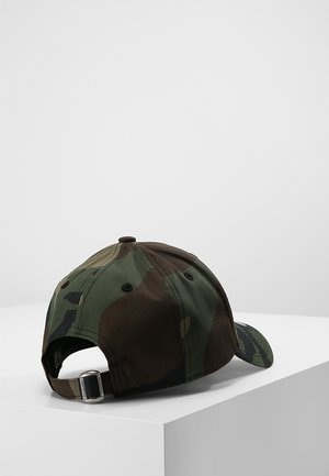 Casquette de baseball à motif camouflage avec une sangle ajustable en métal reposant sur le côté sur une surface blanche contre un fond uni.