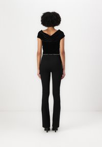 Top de terciopelo negro con un escote amplio y mangas cortas, combinado con pantalones de campana negros de cintura alta y tacones de aguja. Detalle de cinturón de cadena.