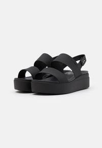 Black platform sandals with wide crossed straps and an adjustable heel strap. Textured footbed and smooth matte finish. Lightweight design.
