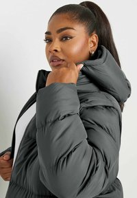 Chaqueta de plumas gris con un alto cuello y capucha ajustada. La tela parece suave con un patrón acolchado, con un zipper visible.