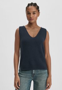 Marineblauwe gebreide mouwloze top met een V-hals, gestructureerd patroon en een rechte zoom, gecombineerd met lichtblauwe jeans.